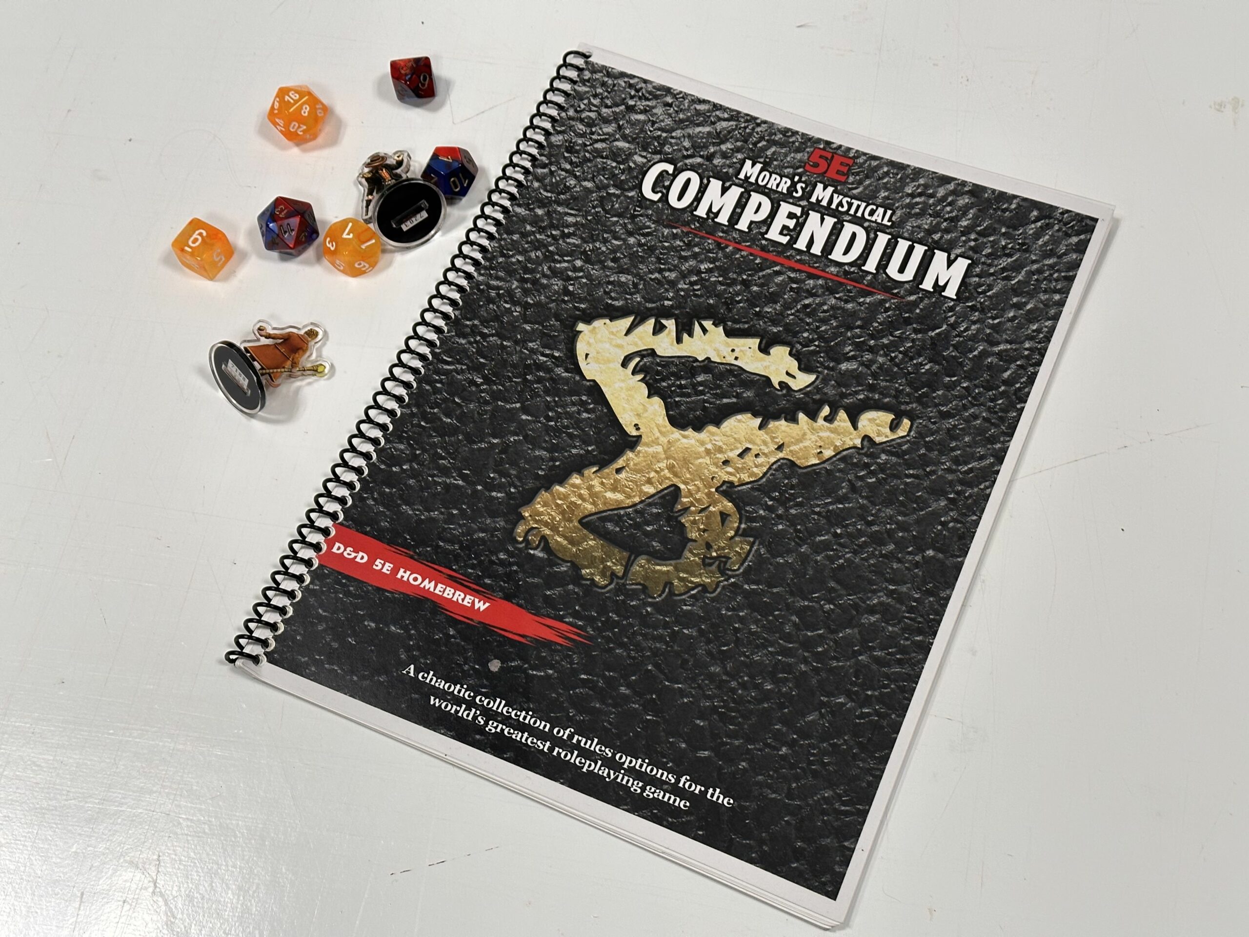 A photo of the printed book, next to some dice and miniatures made in Heroforge.com